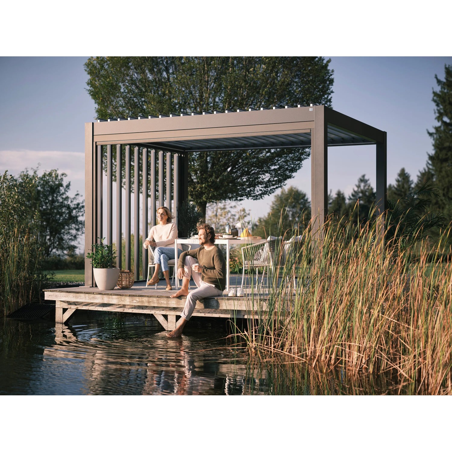 Biohort Pergola in Dunkelgrau/Silber-Metallic auf Holzsteg am See mit sitzenden Personen.