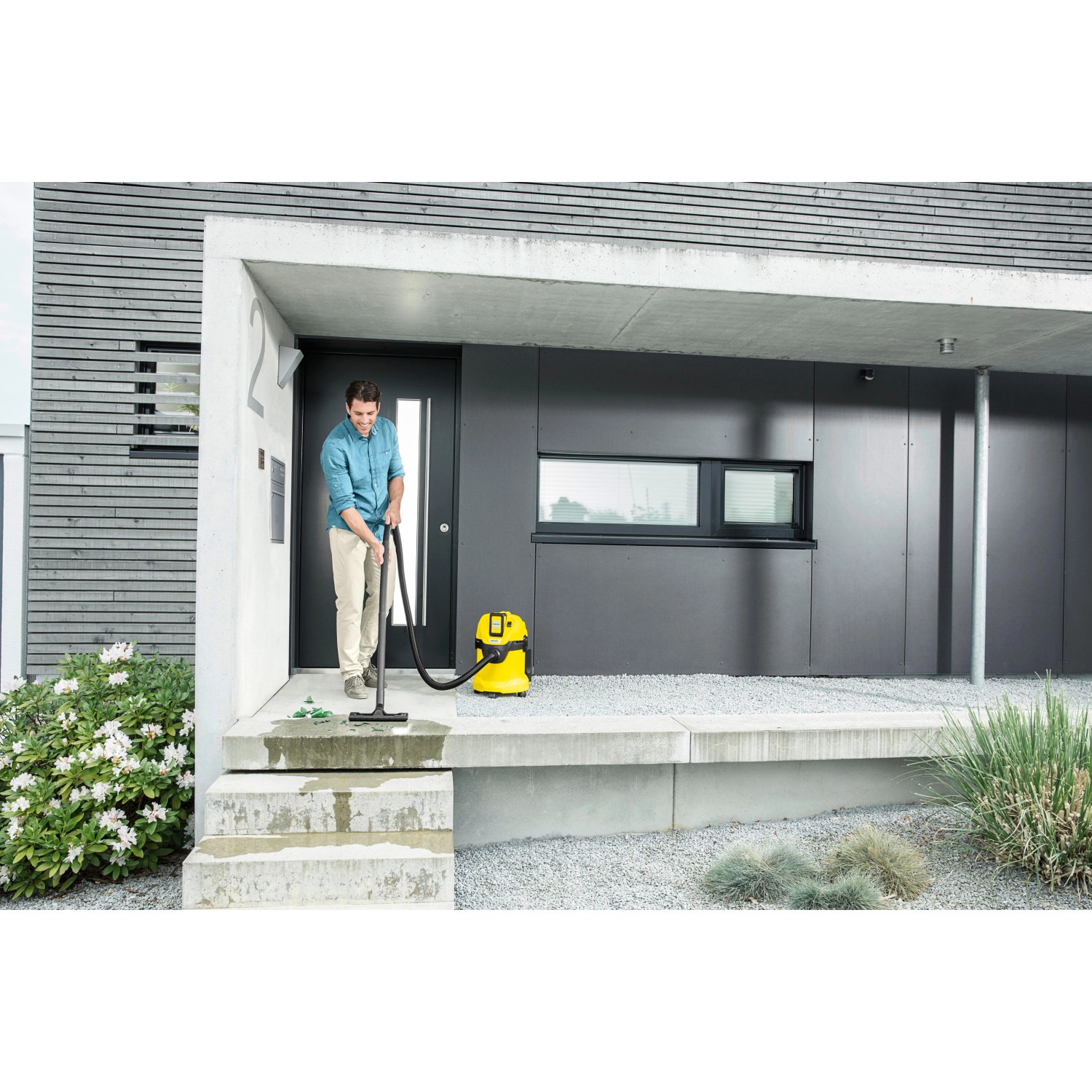 Mann saugt mit gelbem Kärcher Akku-Mehrzwecksauger WD 3 Battery eine Treppe vor dem Haus.