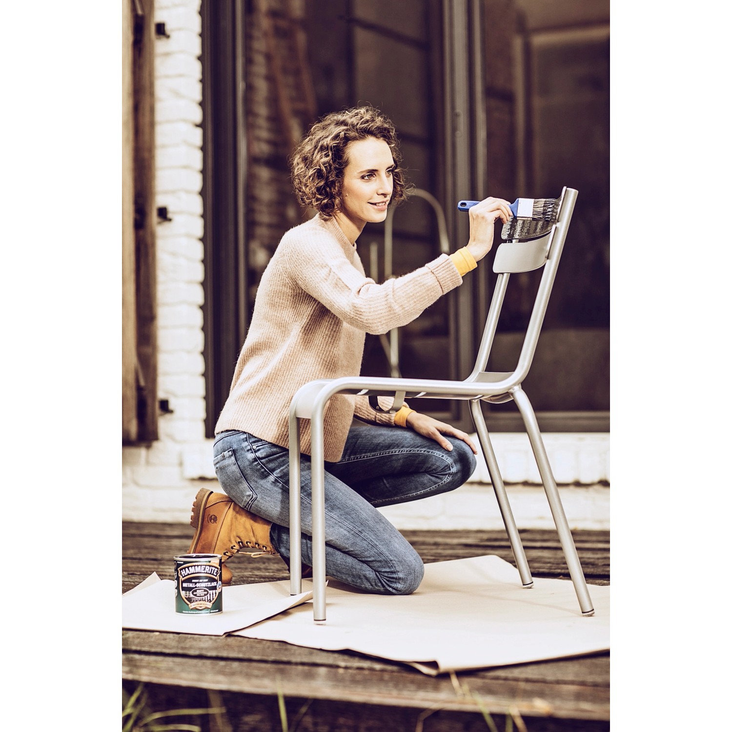 Frau streicht Metallstuhl mit Hammerite Ultima Metallschutzlack in Verkehrsgrau.