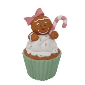 Dekorative Weihnachtsfigur: braunes Lebkuchenmädchen mit rosa Schleife auf weißem Cupcake mit grüner Form, Zuckerstange.