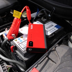 Rotes Mini Lithium Power Pack 200A mit Krokodilklemmen und LED-Arbeitsleuchte auf Autobatterie.