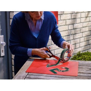 Frau schneidet Tesa Montageband für Mauerwerk mit Schere auf roter Unterlage.