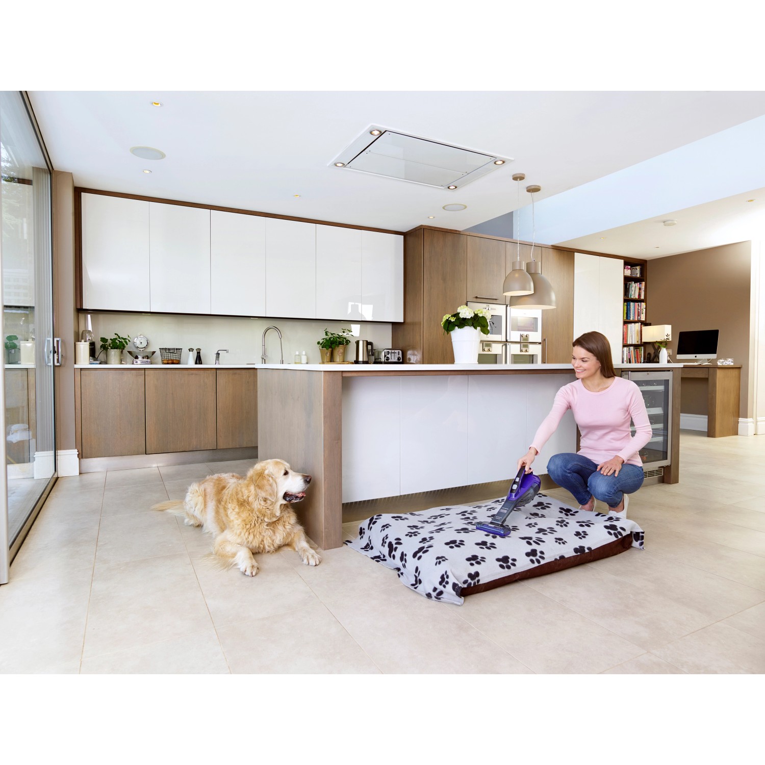 Frau saugt Tierbett mit Black+Decker Akku-Handstaubsauger Pet DVA325JP7, Hund liegt daneben.