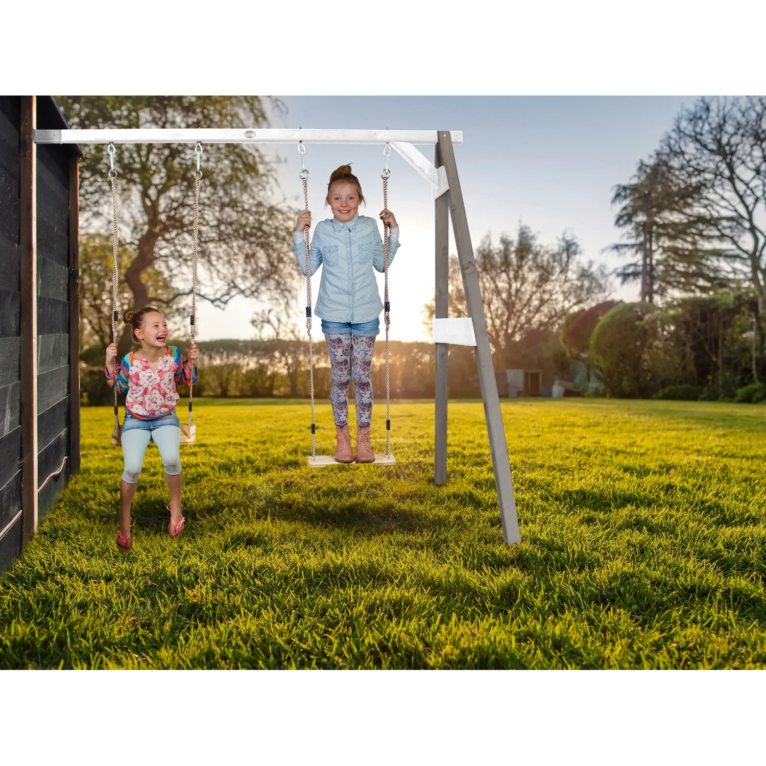 Axi Doppel-Anbauschaukel in Grau und Weiß mit zwei Kindern beim Schaukeln im Garten.