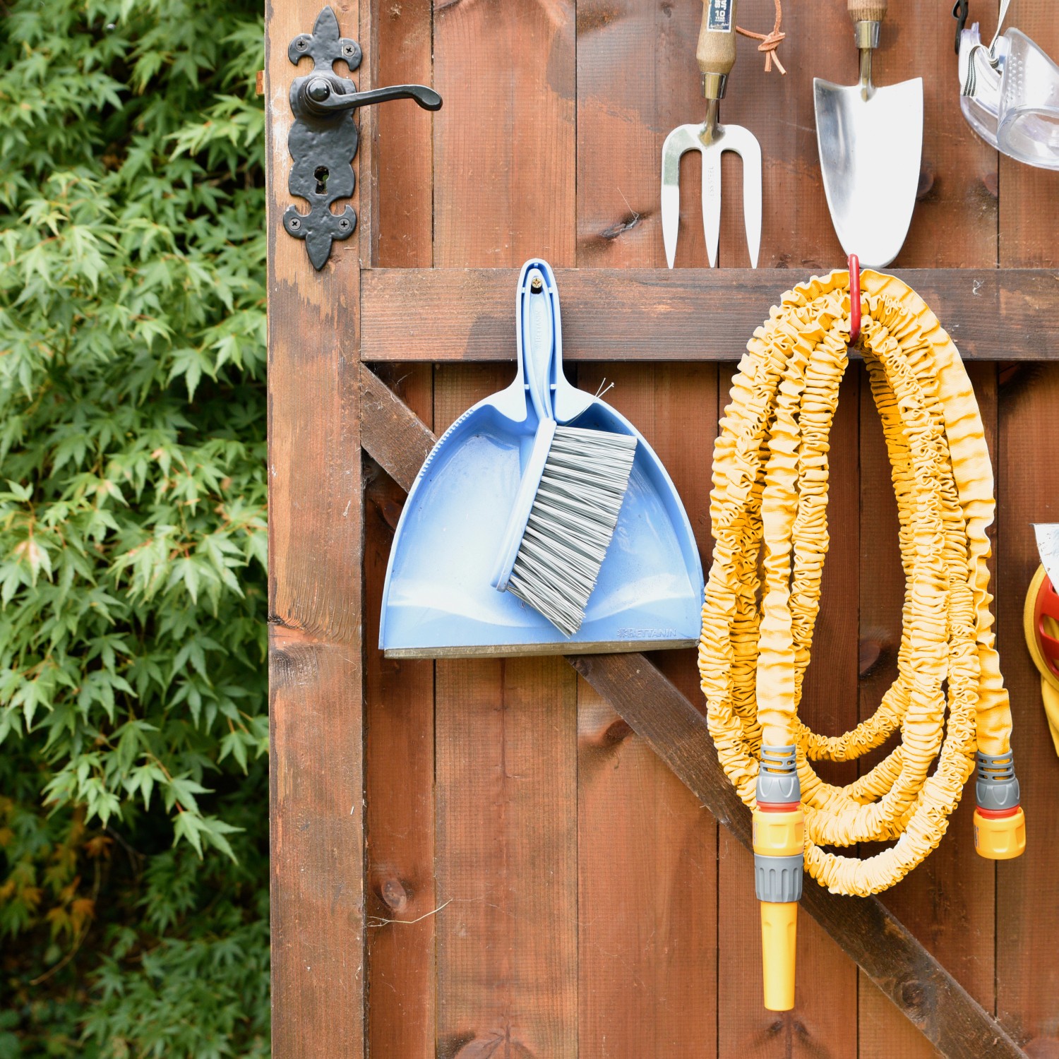 Gelber Hozelock SuperHoze Expansions-Gartenschlauch (15m) hängt an einer Holzwand mit Gartengeräten.