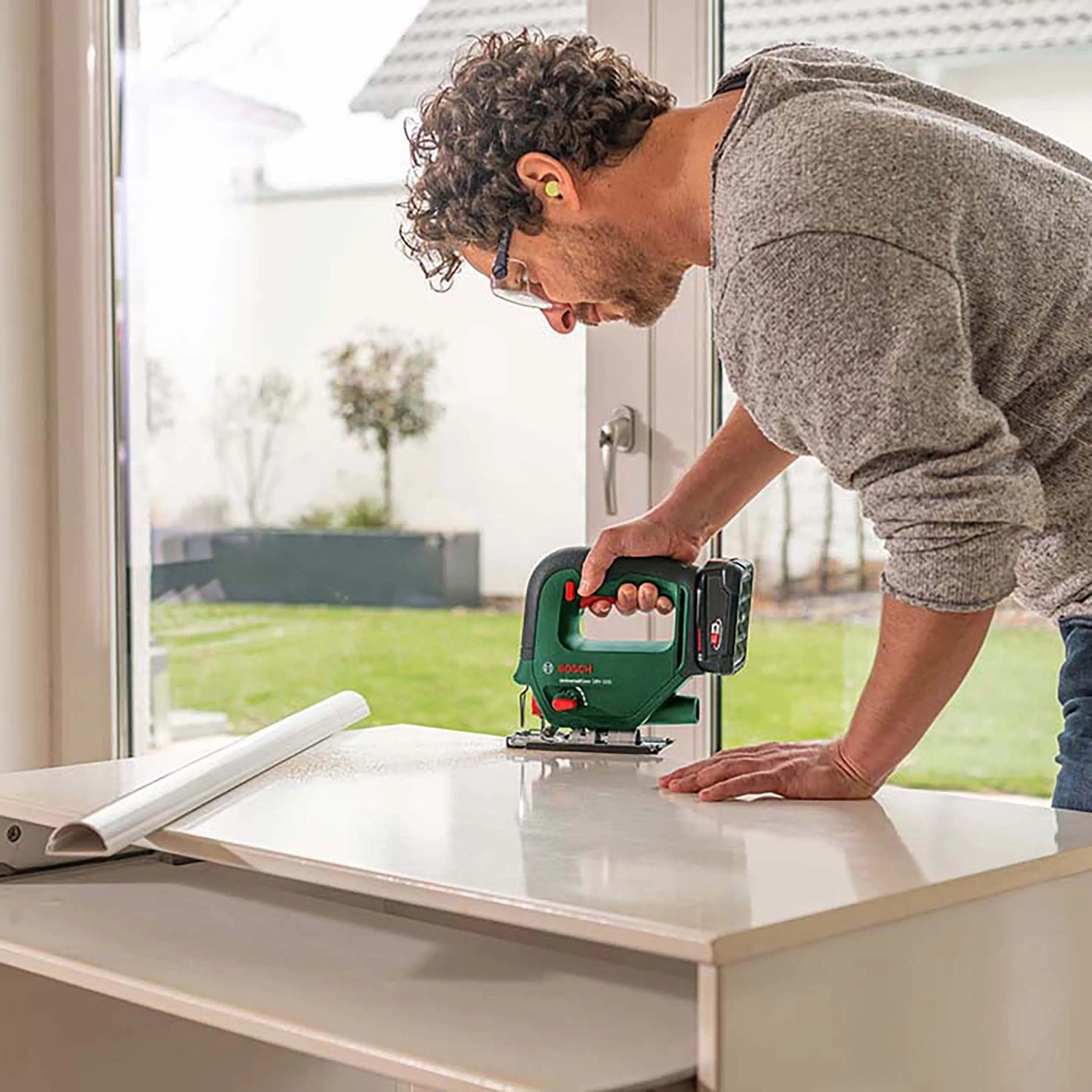 Mann sägt mit Bosch Akku-Stichsäge UniversalSaw 18V-100 ein Werkstück. Stichsäge für Holz-, Kunststoff- & Metallarbeiten.