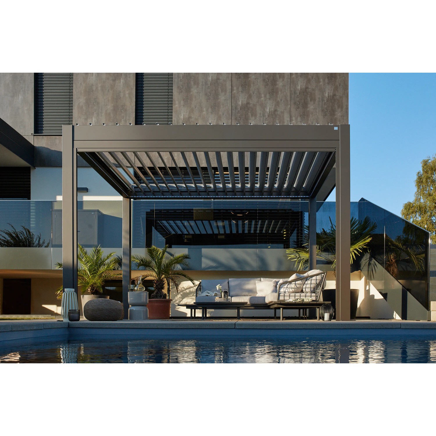 Moderne, dunkelgraue Biohort Pergola mit Lamellen und Sitzgruppe am Pool.