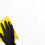Hand mit schwarzem Einmalhandschuh reinigt weiße Fliesen mit gelbem Tuch. Latexfrei, Größe S, 50 Stück.