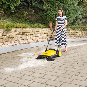 Frau kehrt mit gelber Kärcher Kehrmaschine S4 Twin Pflastersteine im Garten.