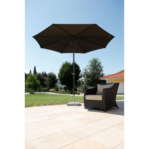 Brauner Schneider Marktschirm Korsika (Ø 320 cm) mit Kurbel neben einem Sessel im Garten.