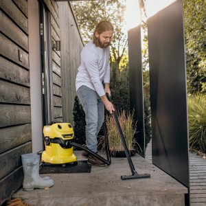 Mann saugt mit gelbem Kärcher Nass-Trockensauger WD 4 V-20/5/22 eine Terrasse.