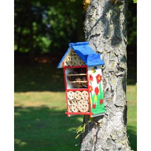Bemaltes Insektenhotel-Bausatz für Kinder (FSC®) am Baum. Nützlingshotel mit blauen Dach und bunten Blumen.