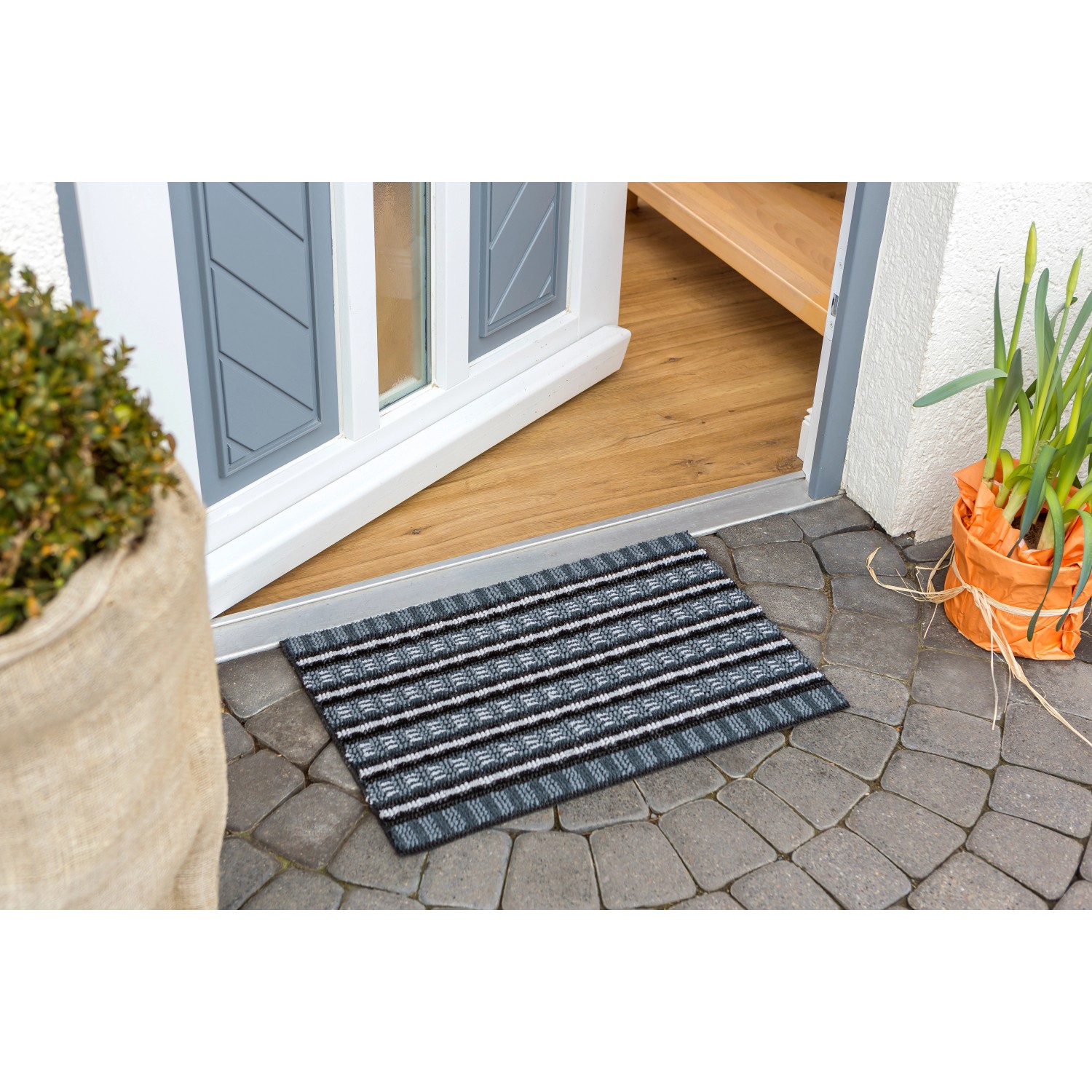 Astra Fußmatte Poly Brush, 40x60 cm, schwarz-silber gestreift, vor einer Haustür.
