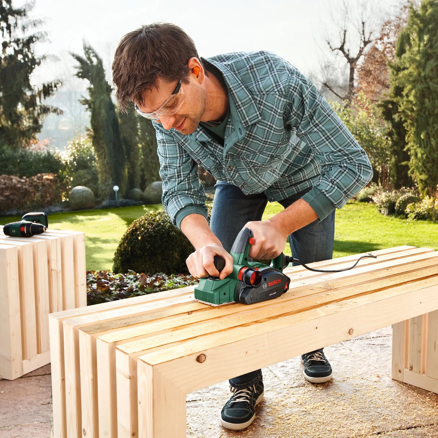 Mann hobelt Holz mit Bosch Elektrohobel PHO 2000 im Garten. Hobel für präzise Holzbearbeitung.