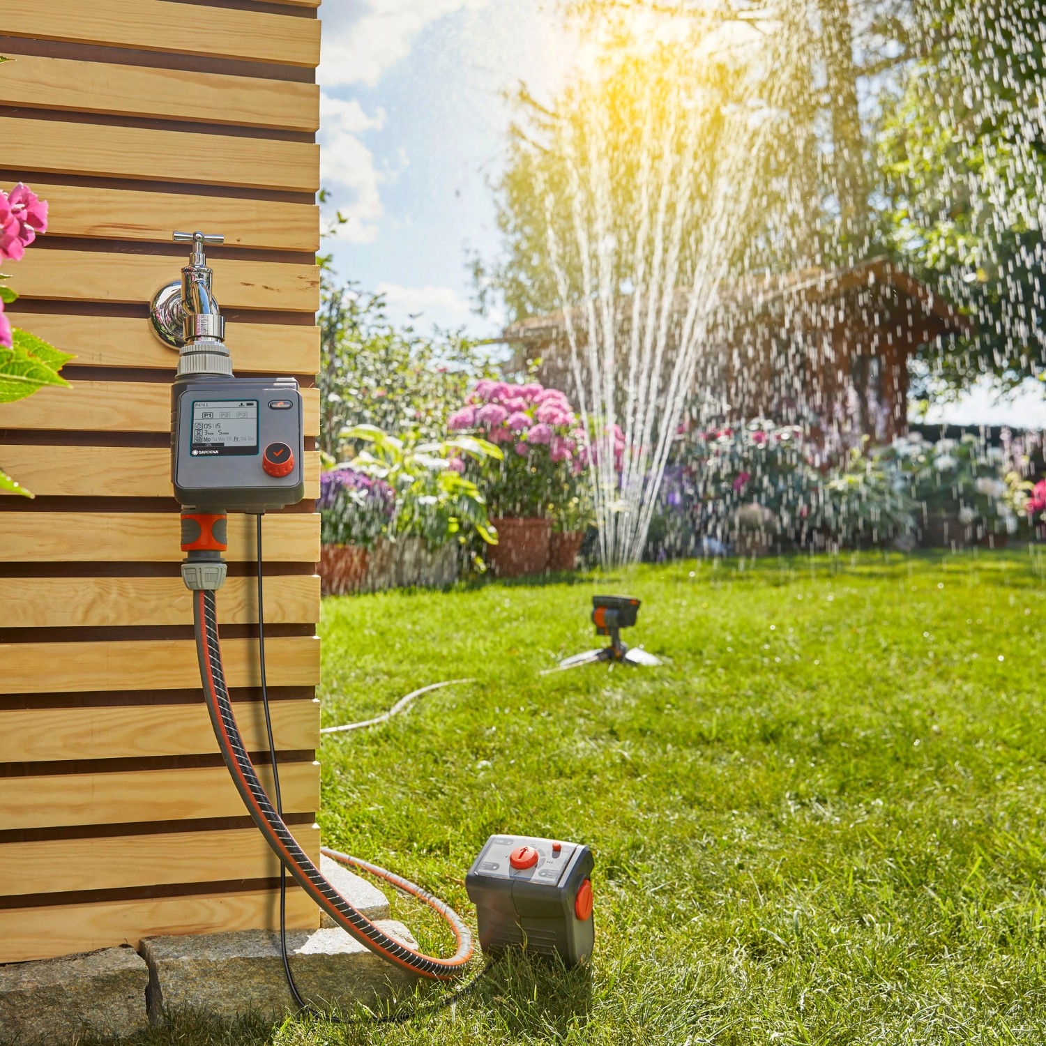 Gardena Bewässerungscomputer Select am Wasserhahn mit Rasensprenger im Garten.