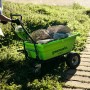 Grüne Greenworks Akku-Schubkarre G40GC mit Steinen beladen im Garten.