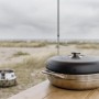 Petromax Camping Backofen aus Edelstahl auf Tisch, Strand im Hintergrund.