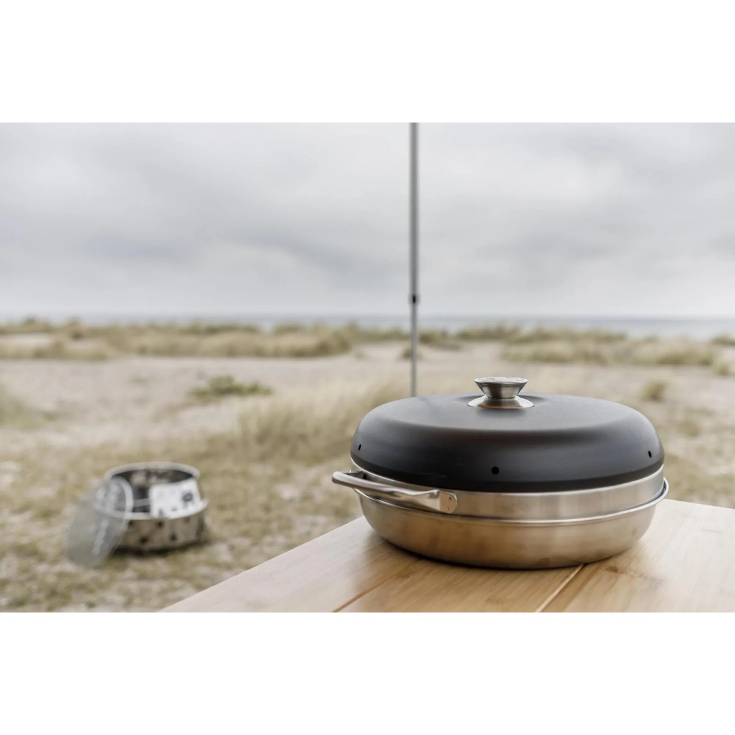 Petromax Camping Backofen aus Edelstahl auf Tisch, Strand im Hintergrund.