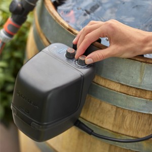 Gardena Akku-Regenfasspumpe 2400 ComfortAutomatic Set am Regenfass mit Hand an Bedienelement.