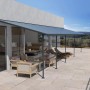 Graue Palram Canopia Terrassenüberdachung Sierra (1035x295cm) auf Terrasse mit Gartenmöbeln.