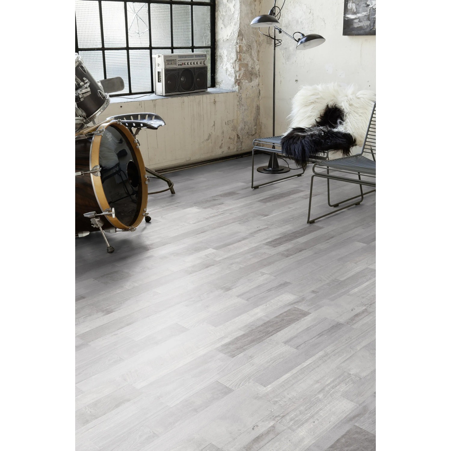Heller Laminatboden im Pinie Sea Pine Dekor, verlegt in einem Raum mit Schlagzeug und Stühlen.