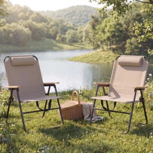 Zwei creme klappbare Campingstühle mit Bambus-Armlehnen und Kopfstützen auf Gras am See. Perfekt für Outdoor & Garten.