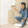 Frau streicht Wand mit Farbroller, LUX Auslegepapier schützt den Boden.
