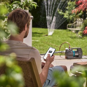 Gardena Haus- und Gartenautomat 5000 Silent Comfort mit App-Steuerung und Gartenbewässerung im Hintergrund.