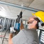 Mann bohrt mit Bosch Professional Bohrhammer GBH 2-28 F in Decke, Baustelle im Hintergrund.