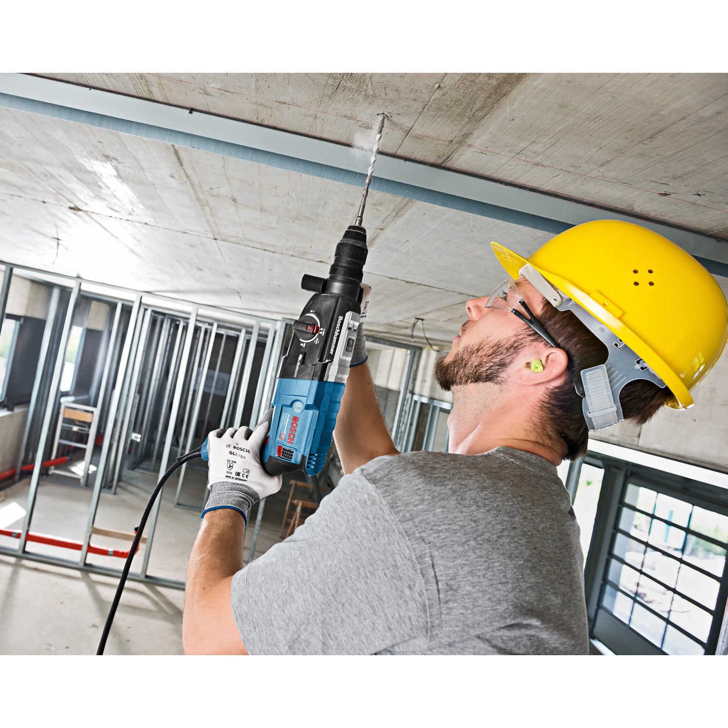 Mann bohrt mit Bosch Professional Bohrhammer GBH 2-28 F in Decke, Baustelle im Hintergrund.