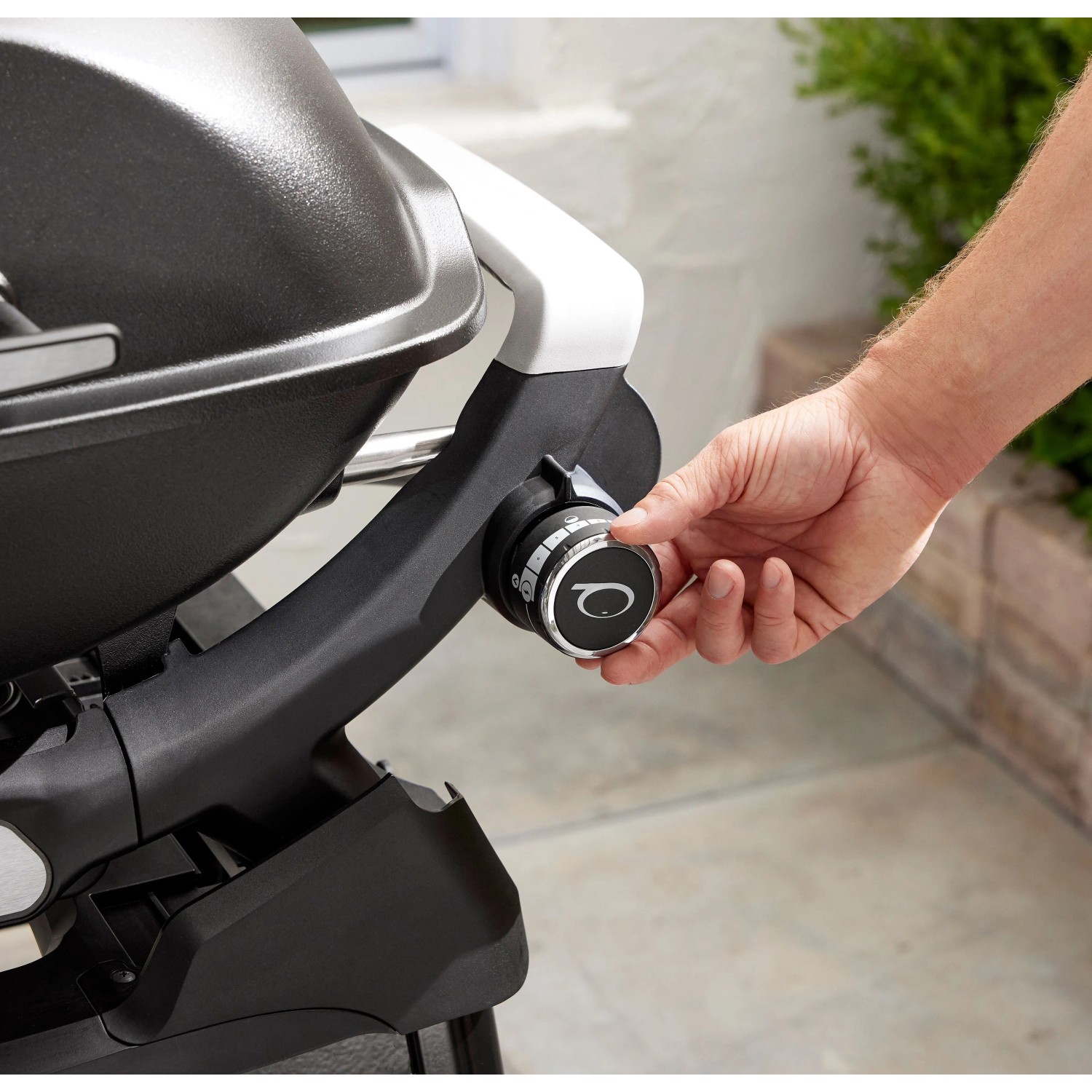 Detailaufnahme: Weber Gasgrill Q2200N mit Stand, schwarzer Grill mit Hand am Bedienknopf.