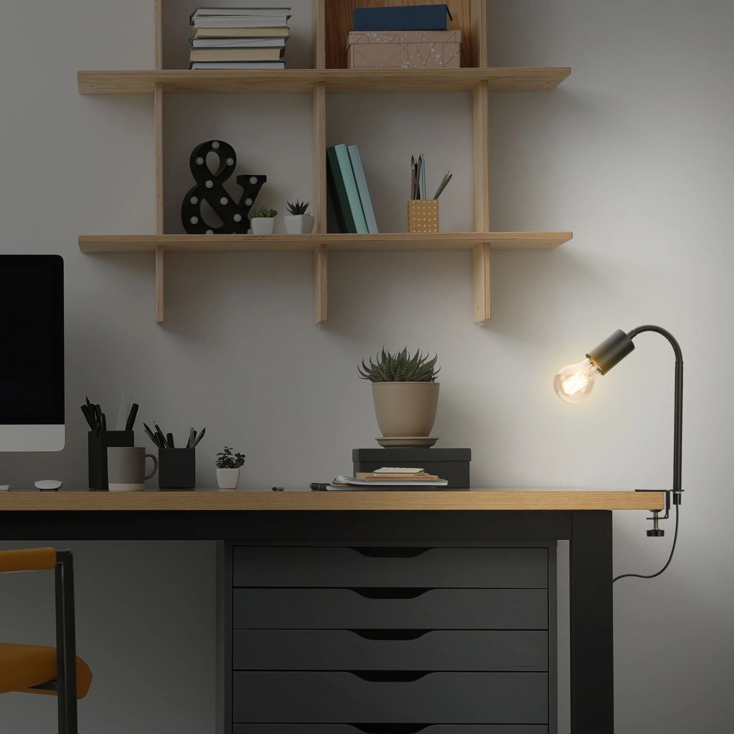 Schwarze Briloner Klemmleuchte Krampo am Schreibtisch mit Regalen und Dekoration.