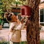 Elho Vogelfutterhaus Cosy, rot-weiß, am Baum befestigt, mit Mädchen im Garten.