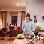 Philips Hue Starter-Set: Frau schneidet Gemüse in warmweiß beleuchteter Küche, Freunde im Hintergrund.