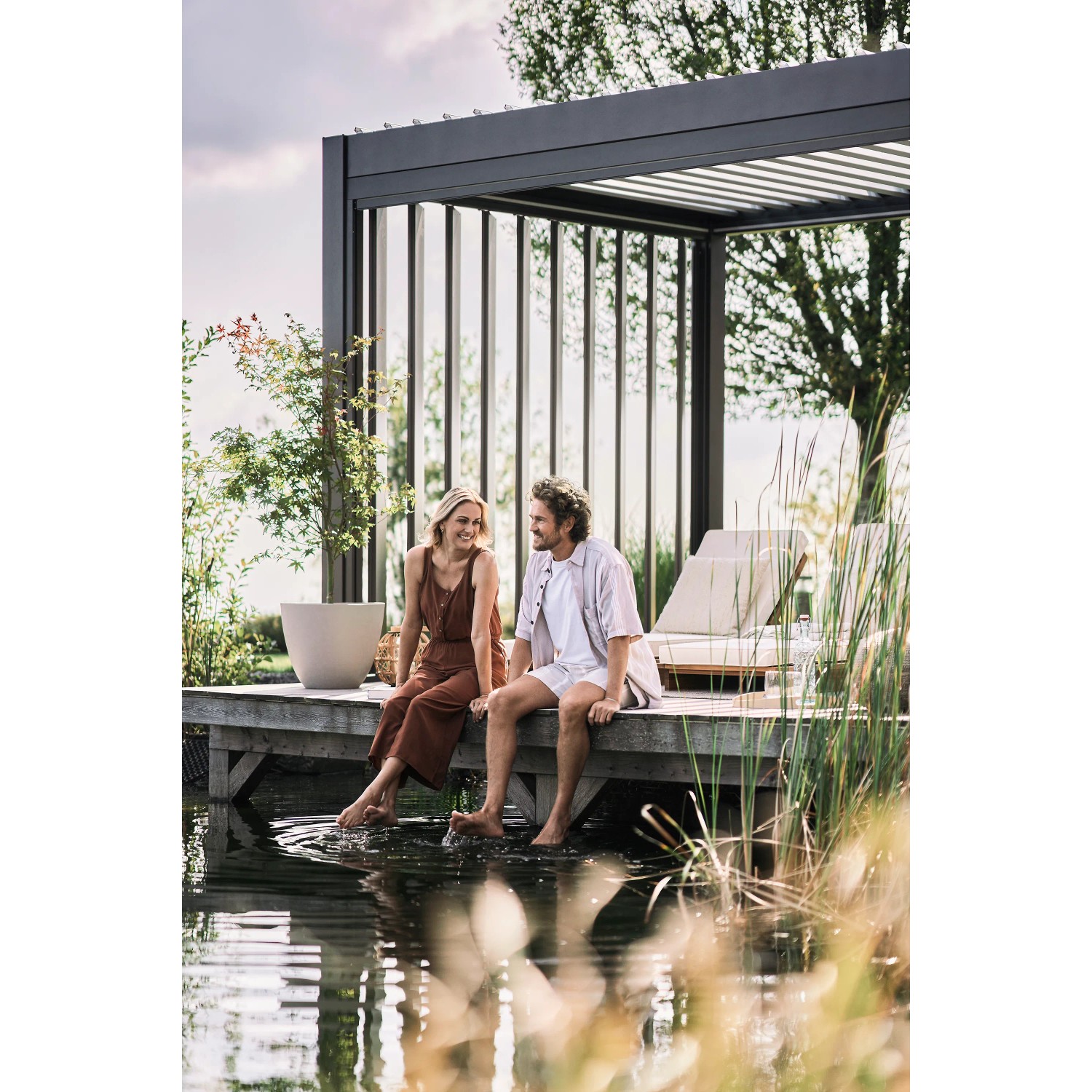 Biohort Lamellenseitenwand in Dunkelgrau-Metallic an Pergola mit Paar am Wasser.