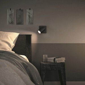 Schwarzer, drehbarer Kosipo Spot an Schlafzimmerwand, beleuchtet Nachttisch. Modernes Design für gezieltes Licht.