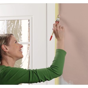 Frau streicht Wand mit Tesa Malerband für saubere Kanten. Beige Abdeckband für Farbarbeiten.