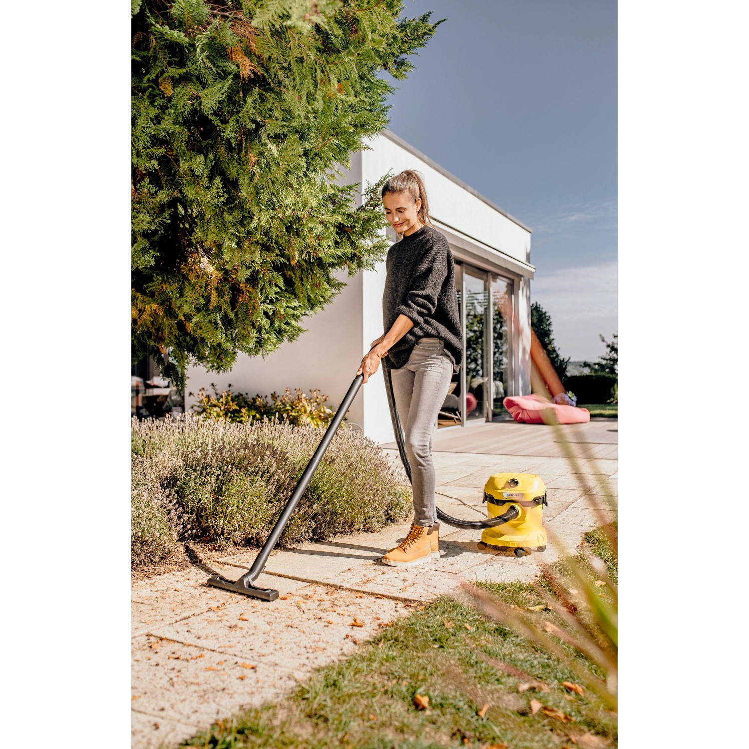 Frau nutzt gelben Kärcher WD 2 Plus Nass-Trockensauger im Außenbereich.