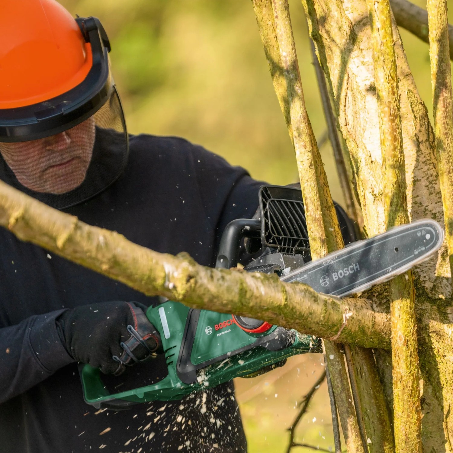 Mann sägt Ast mit Bosch Akku-Kettensäge PKE18V-30-28. Akku-Kettensäge im Einsatz.