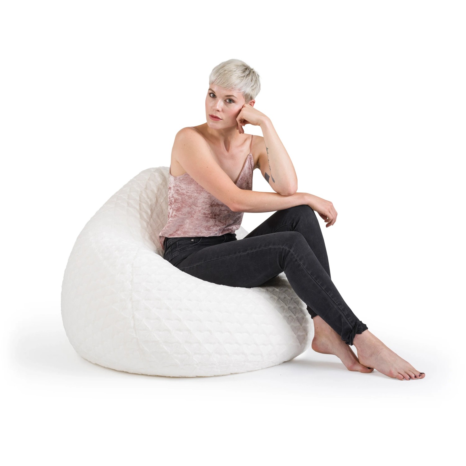 Frau sitzt entspannt im weißen Sitting Point Sitzsack BeanBag Fluffy mit Herzmuster.