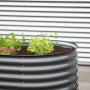 Anthrazitfarbenes Westmann Hochbeet Oval aus Metall mit Bepflanzung vor einer Wand.