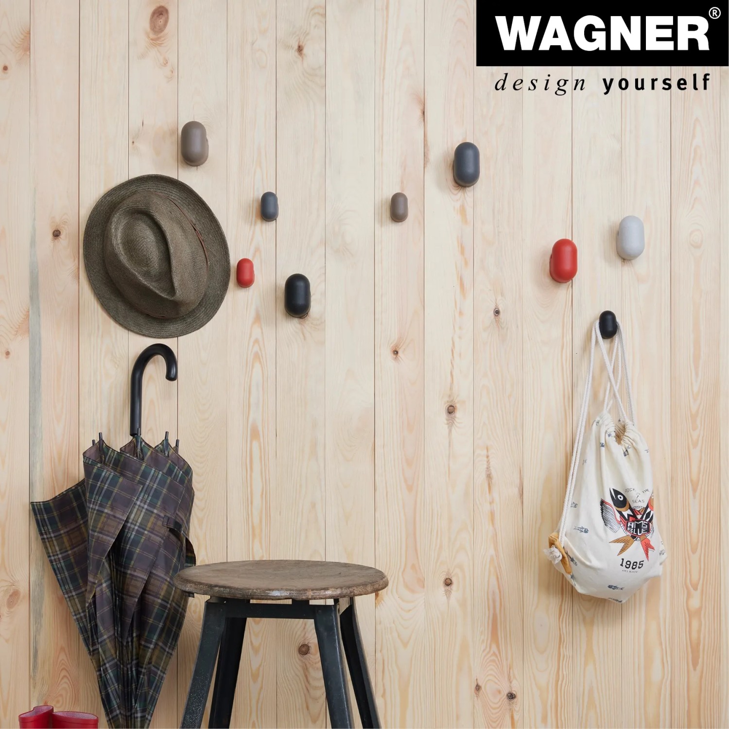 Wagner Wandhaken-Set Pill WH 0421, 4 Haken in Taupe, Koralle, Grau und Schwarz an einer Holzwand mit Accessoires.