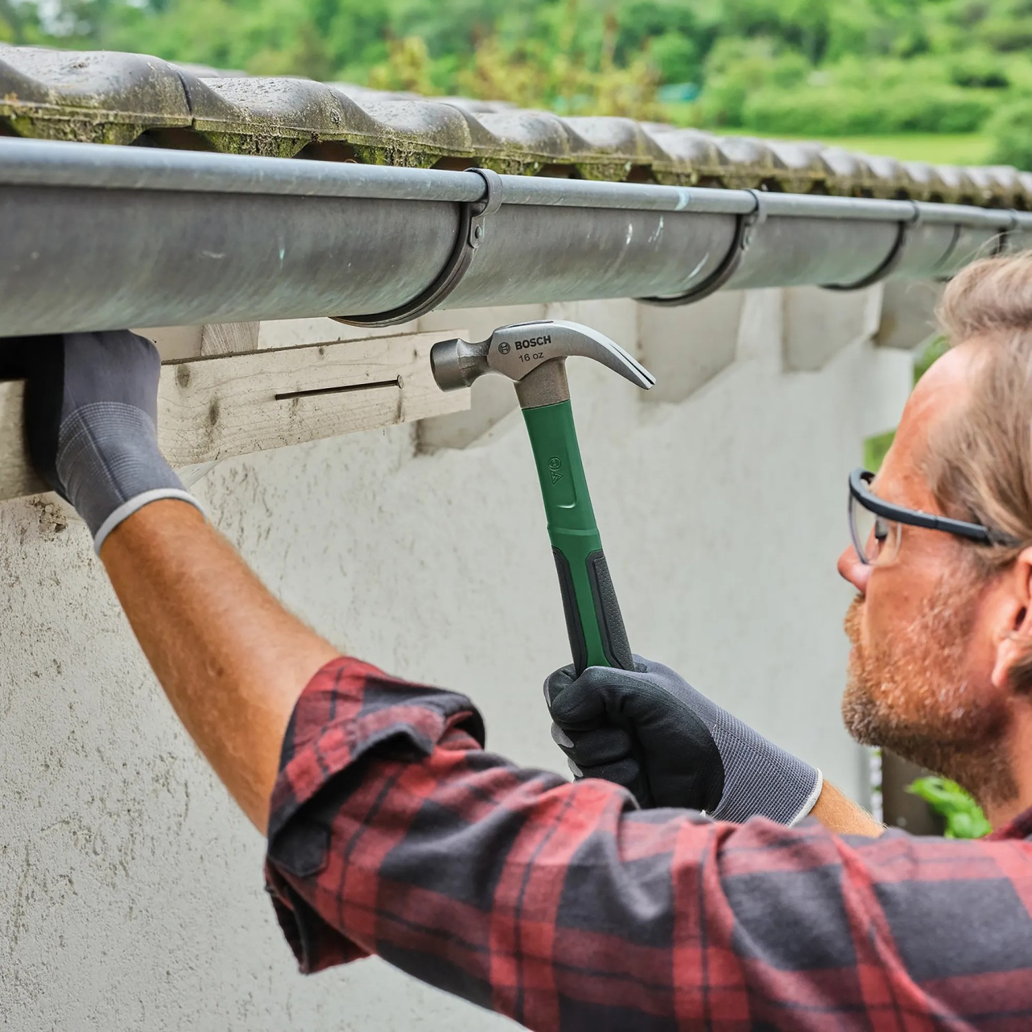 Mann arbeitet mit Bosch Klauenhammer (450g) an Dachrinne. Der Hammer hat einen grünen Griff.