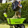 Grüne Greenworks Akku-Schubkarre G40GC mit Gras befüllt, Frau leert Fangkorb.