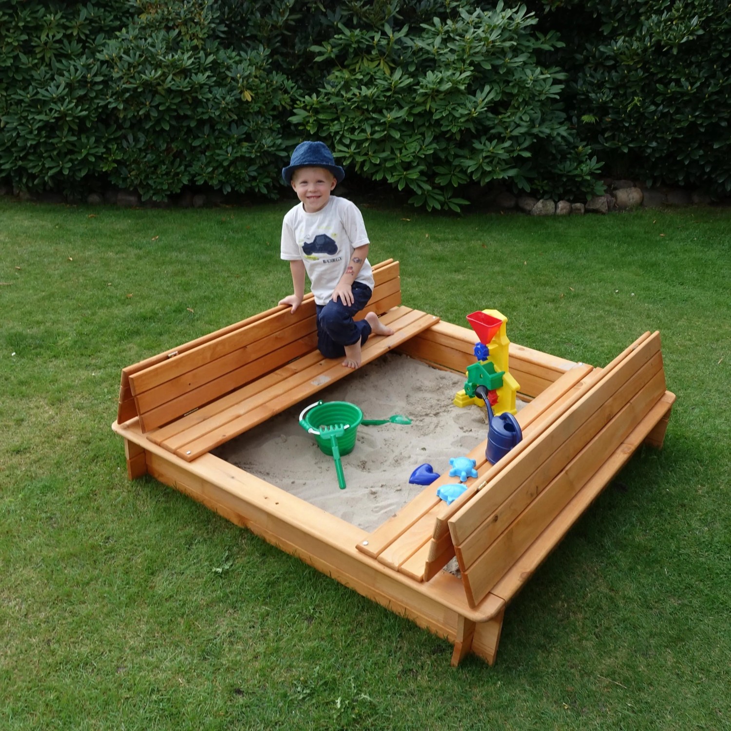 Quadratischer Sandkasten Donald 140x140 cm mit klappbarer Abdeckung und integrierten Sitzbänken.