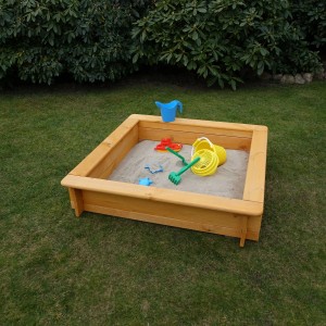 Quadratischer Sandkasten Tessa 100x100 cm aus Holz mit Spielzeug im Garten.