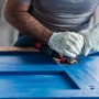 Anwender schleift blaue Holzoberfläche mit Bosch Expert Schleifplatte AVZ90 RT4 am Multifunktionswerkzeug.