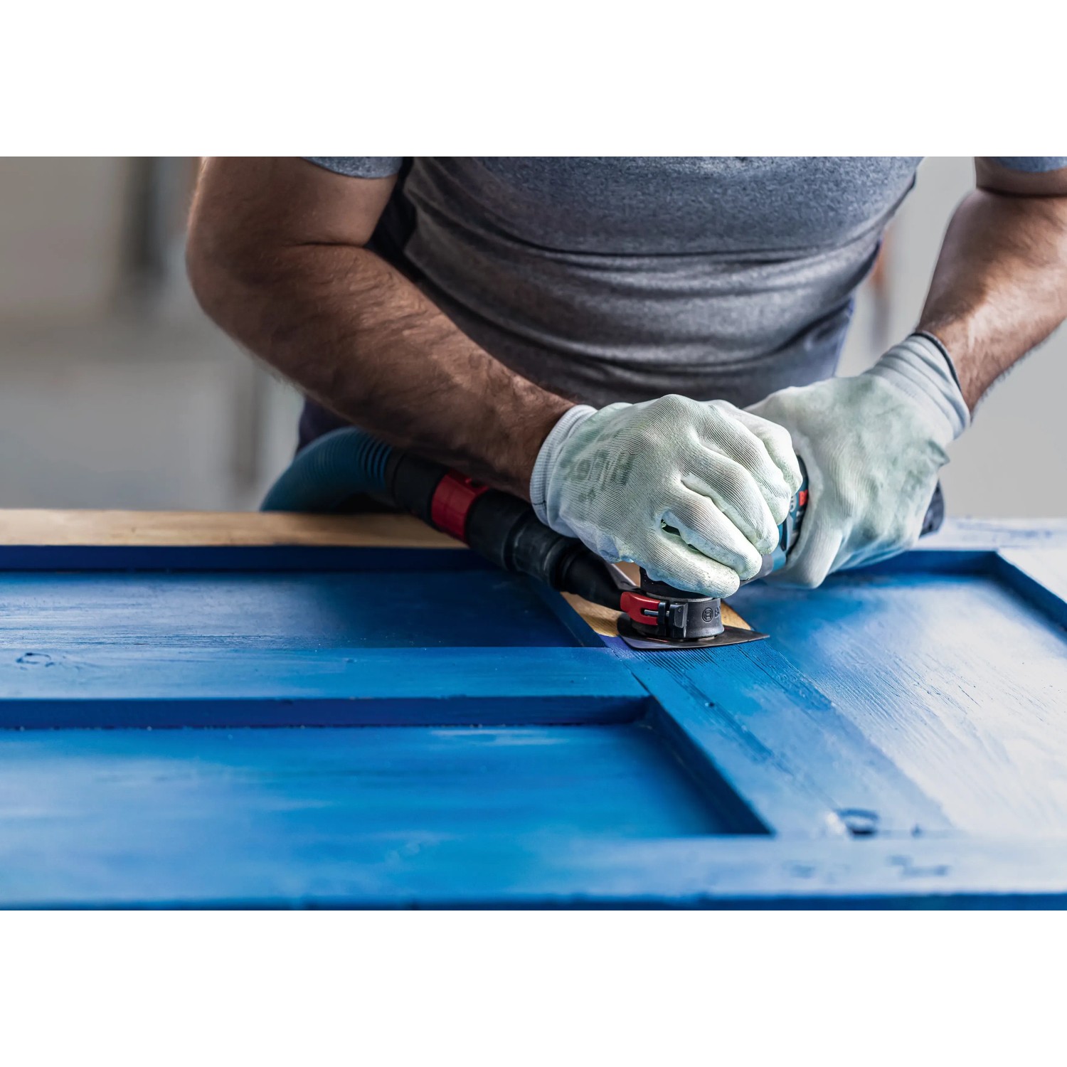 Anwender schleift blaue Holzoberfläche mit Bosch Expert Schleifplatte AVZ90 RT4 am Multifunktionswerkzeug.