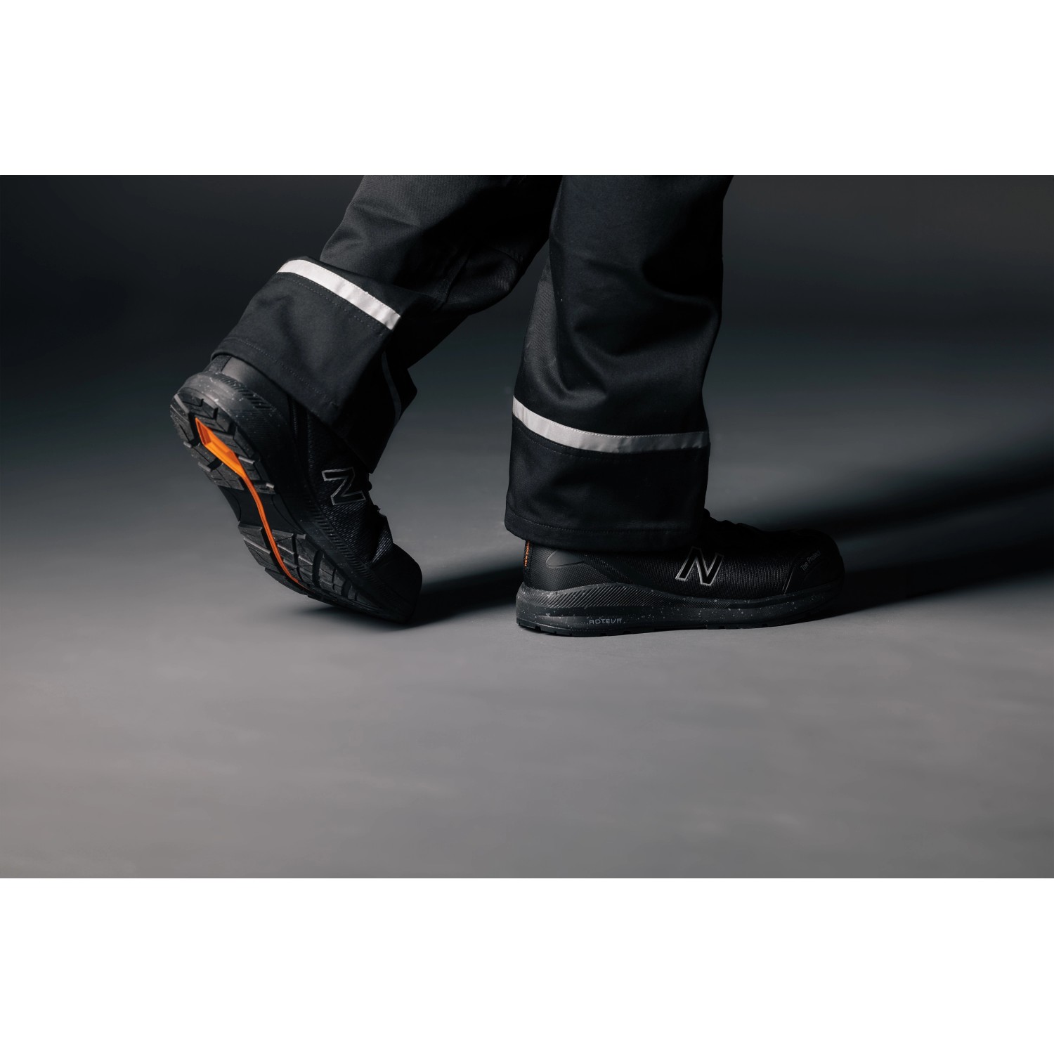 New Balance Logic S1 PL Sicherheitsschuhe, schwarz-orange, getragen mit Arbeitshose.