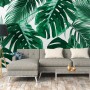 Fototapete mit Palmen- und Monstera-Blättern in Grün und Weiß hinter einem Wohnbereich.